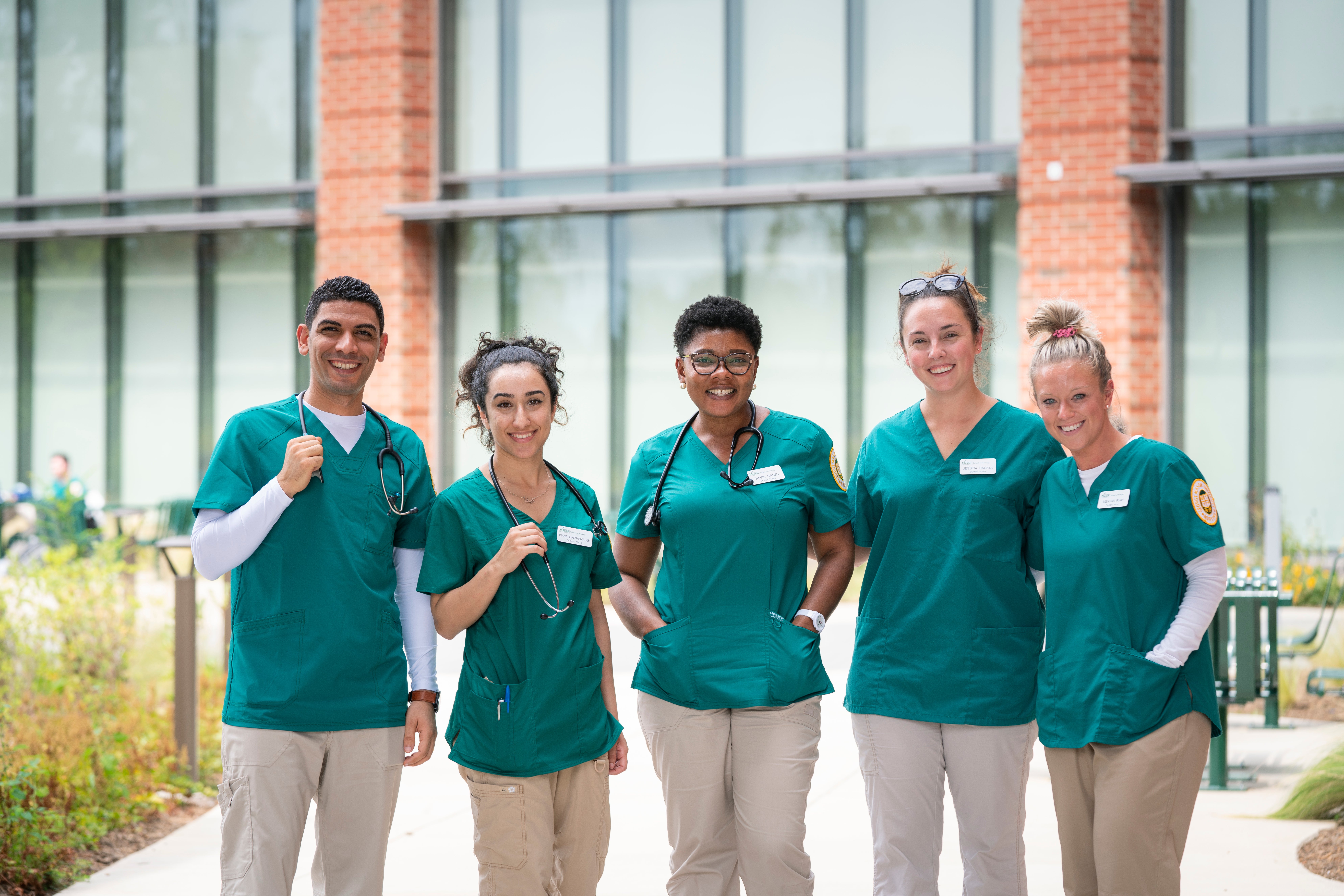 Image of five nurses standing outside of the School of Nursing building.